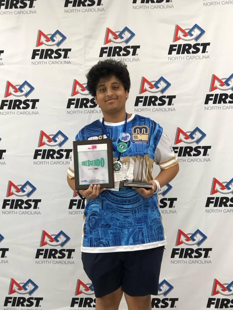 Arvin in a team jersey holding awards in front of a FIRST North Carolina backdrop