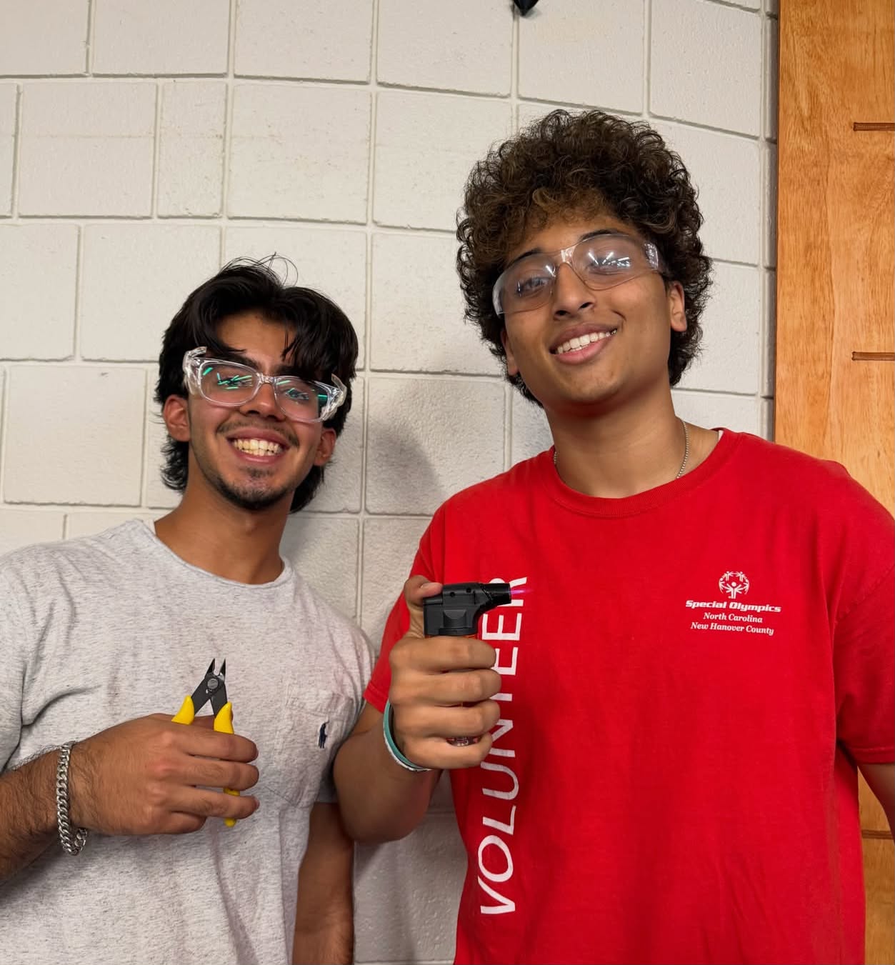 Arvin and a teammate in safety glasses holding a heat gun and wire cutters