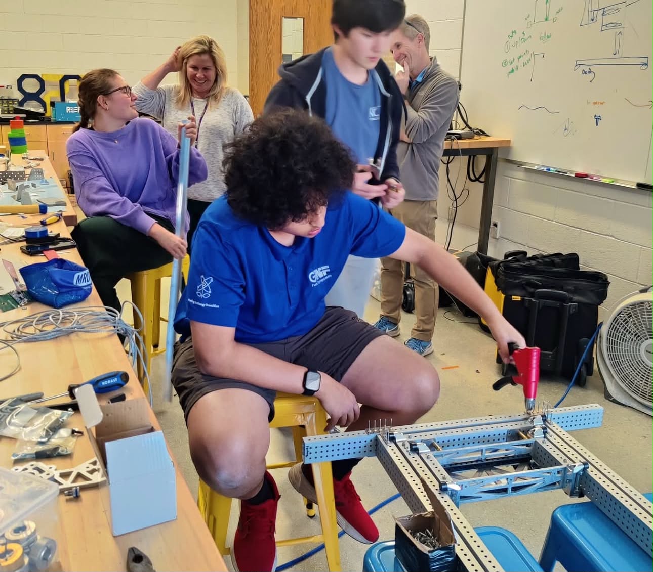 Arvin riveting an aluminum robot chassis in the workshop while teammates and mentors look on