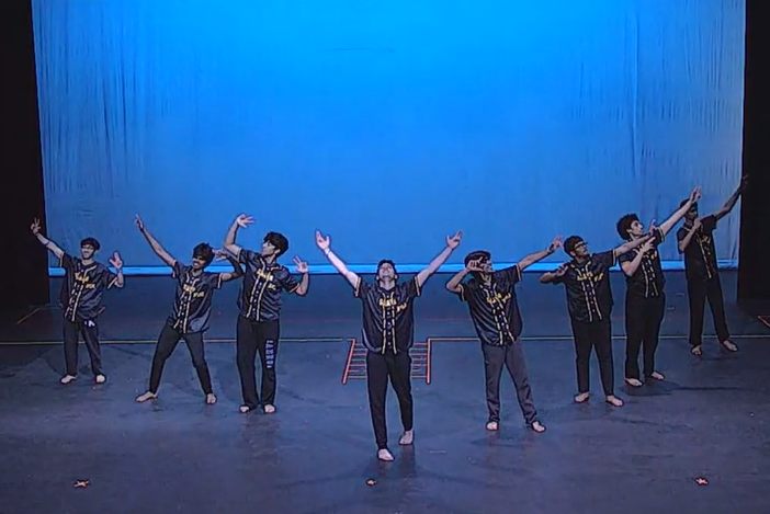 SAATH performing on stage in front of a blue backdrop, arms raised in formation